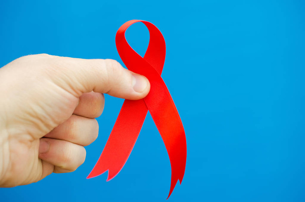 Red folded ribbon in hand on a blue background as a symbol of hemophilia. - Photo, Image