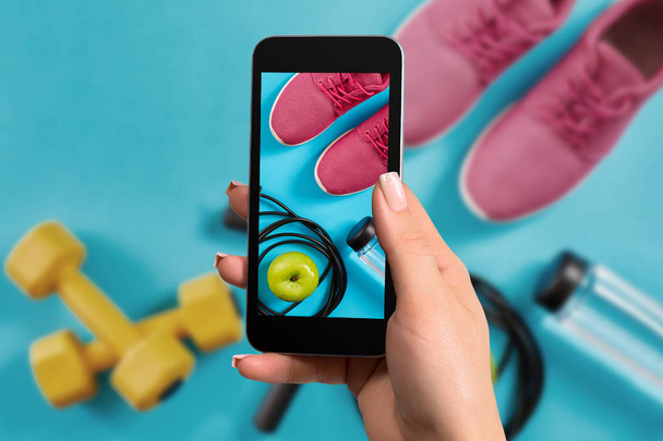 Mano femminile con uno smartphone rende un attrezzo da fitness foto su sfondo blu
 - Foto, immagini