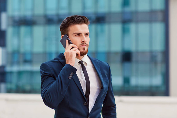 Businessman with a beard talking on the phone against a building - Фото, зображення