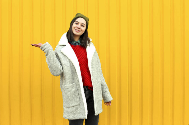 Millenial girl im fashionable clothes having a good time, making funny faces near bright yellow urban wall. - Foto, Imagen