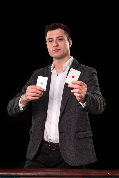 Kaukasische jongeman dragen pak bedrijf twee azen in zijn handen op zwarte achtergrond. Gokken concept. Casino - Foto, afbeelding