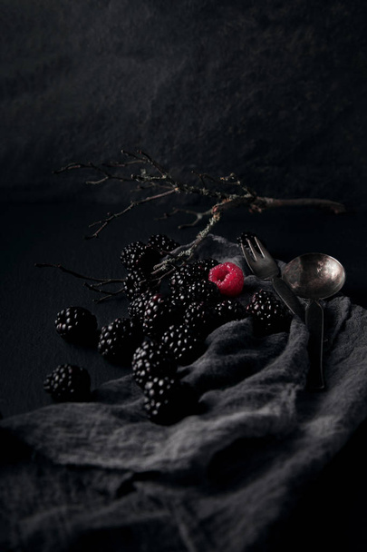 monochrome food picture of blackberries and one red raspberry on a napkin and slate plate kitchen table can be used as background - Zdjęcie, obraz