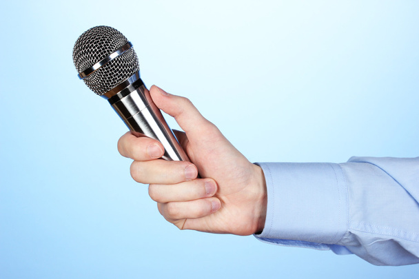 Male hand with microphone on blue background - Zdjęcie, obraz