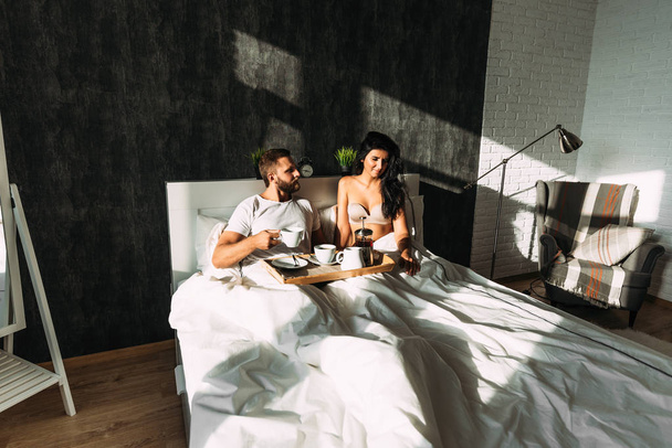 Loving couple having breakfast in bed. Guy and girl in bed. Breakfast in bed. Tea in bed. The relationship between a man and a woman. Loving couple. Morning lovers. Family relationships. Good morning - Foto, Bild