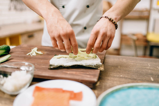 Cuoco maschile che fa sushi con avocado sul tavolo di legno. Cucina giapponese tradizionale, frutti di mare
 - Foto, immagini