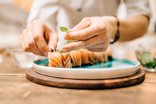 cocinero masculino decorando rollo de sushi en plato azul. Cocina tradicional japonesa, mariscos
 - Foto, imagen