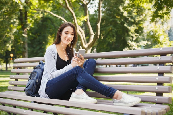 Студент сидит в парке и пользуется смартфоном
 - Фото, изображение
