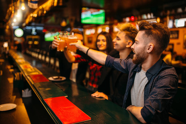 счастливая компания друзей подняла бокалы с пивом в спорт-баре, досуг футбольных болельщиков
 - Фото, изображение