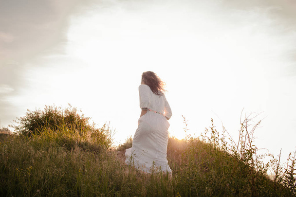 young woman walking on the morning beach in beautiful white dress. Fit female having good time during turing the sunrise. - Fotografie, Obrázek