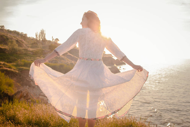 young woman walking on the morning beach in beautiful white dress. Fit female having good time during turing the sunrise. - Valokuva, kuva