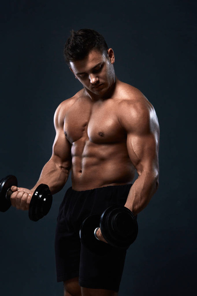 Muscular bodybuilder doing exercises with dumbbell over black ba - Fotó, kép