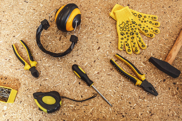 Top view of working tool: noise insulated headphones, tape measure, yellow gloves, wrench, screwdrivers, hammer, pliers, nippers close-up on wooden texture table. Flat lay copy space for advertisement - Photo, Image