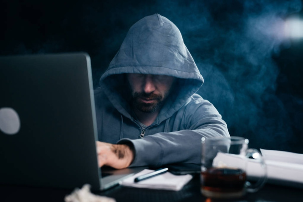 A computer hacker is typing on a laptop in a smoky room. Dark background - Foto, Imagem