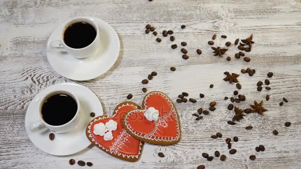Love relations. St. Valentine concept. Top view of Two cups of coffee and two ginger biscuit heart shaped are on wooden background with coffee beans around. Female hand puts I love You message note, 4 - Footage, Video