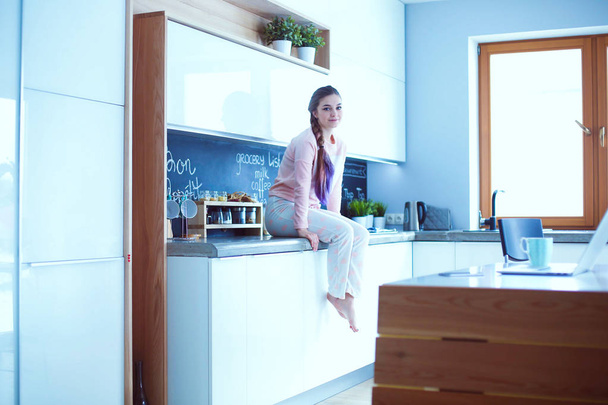 Young woman sitting on table in the kitchen. - Foto, afbeelding