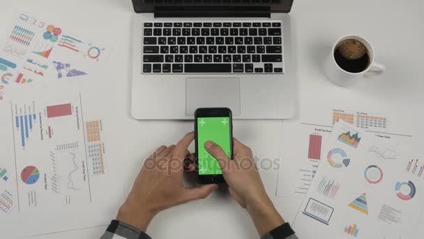 Empresário segurando smartphone com tela verde no fundo da mesa do escritório branco. Mãos masculinas páginas de rolagem
. - Filmagem, Vídeo