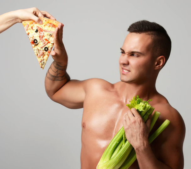Strong muscular athlete men with fresh celery and unhealthy pizza fast food - Фото, зображення