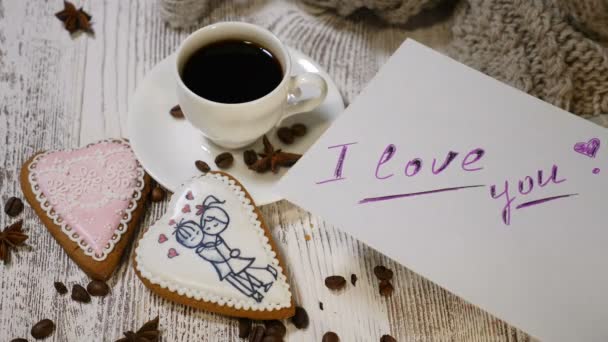Relations de couple. Concept Saint-Valentin. Une tasse de café et biscuit au gingembre avec aiguille à tricoter et fil sur fond en bois. Main met I Love You message note. Tourné en 4 km
 - Séquence, vidéo