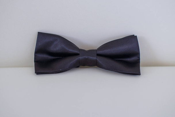 Corbata de lazo sedosa en color sólido azul oscuro o azul marino posicionada sobre un cojín de cuero blanco con fondo blanco, elegante accesorio para atuendo formal
 - Foto, Imagen