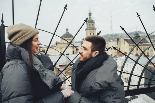 Happy young couple holding hands on roof at city and looking at each other - Фото, зображення