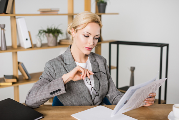 businesswoman with eyeglasses in hand reading newspaper at workplace - Photo, Image