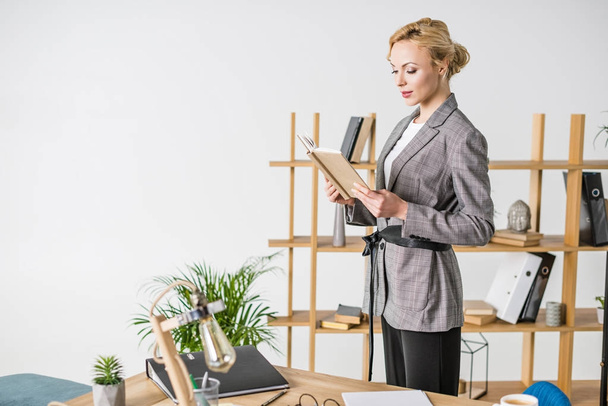 confident businesswoman in suit with notebook standing in office - Fotó, kép