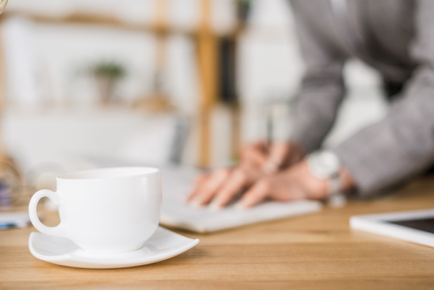 selective focus of cup of coffee on table with businesswoman making notes - Foto, immagini