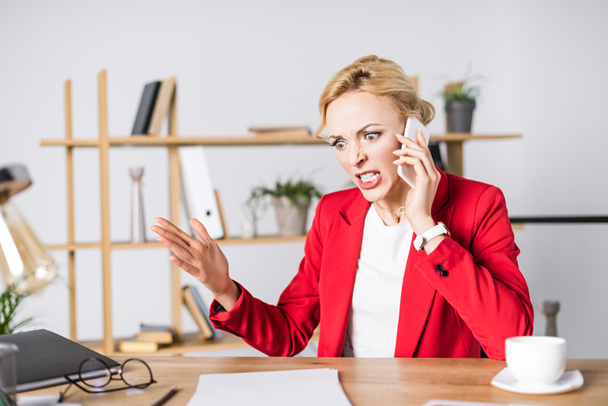 portrait of angry businesswoman talking on smartphone at workplace in office - Foto, Imagem