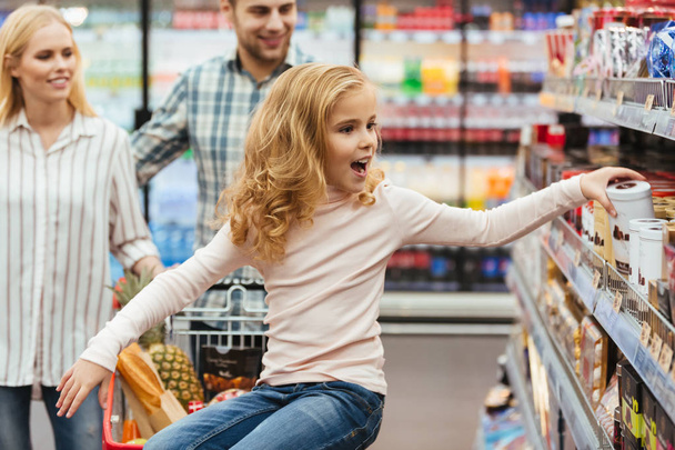 Onnellinen pieni tyttö istuu ostoskärryillä
 - Valokuva, kuva