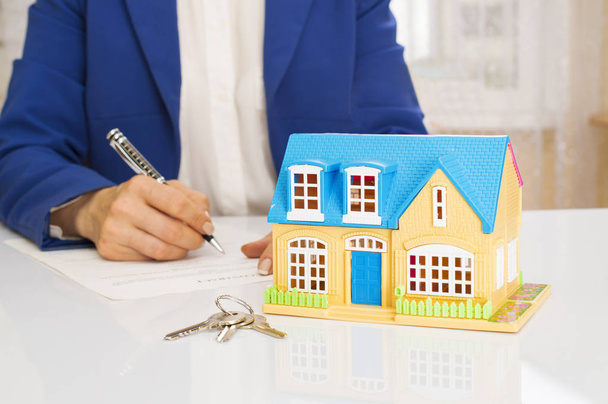 woman with house model and pen signing contract document - Photo, Image