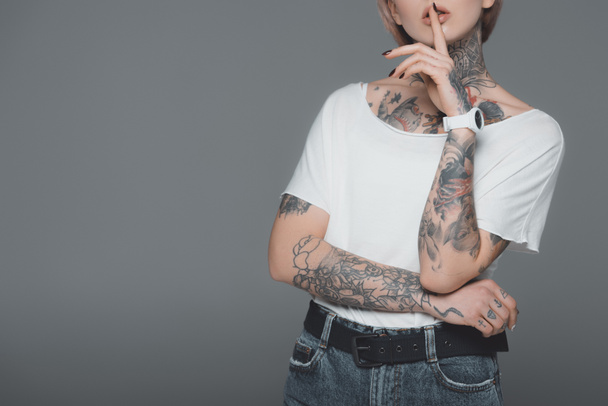 cropped shot of young woman with tattoos gesturing for silence isolated on grey - Foto, imagen