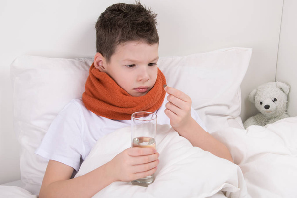 sick boy in bed, drinks medicine pill, washing down with water - Foto, imagen