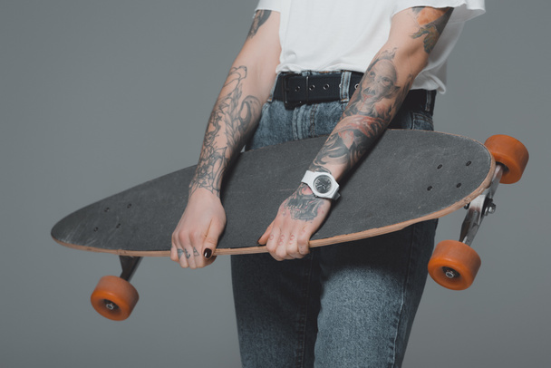 mid section of girl with tattoos holding skateboard isolated on grey - Foto, Bild