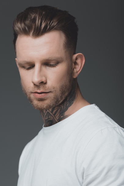 portrait of handsome stylish young tattooed man in white t-shirt looking down isolated on grey - Fotoğraf, Görsel