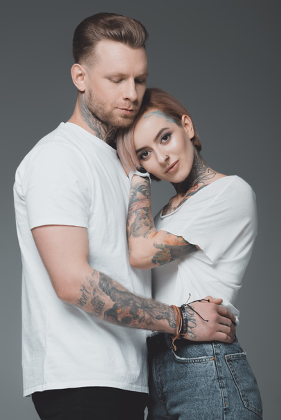 beautiful stylish young tattooed couple in white t-shirts hugging isolated on grey  - Photo, Image