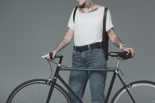 przycięte strzał stylowa dziewczyna z tatuażami, stojąc z rowerem na szarym tle - Zdjęcie, obraz