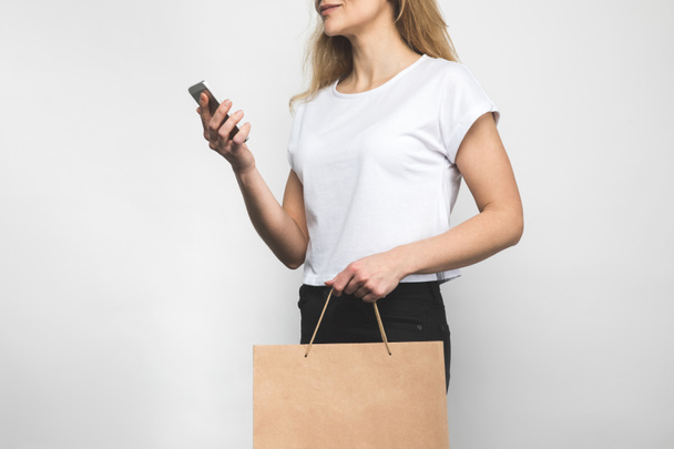 cropped shot of woman in blank t-shirt on white with shopping bag and smartphone - 写真・画像