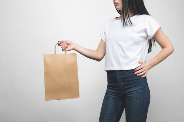 обрезанный снимок молодой женщины в пустой футболке на белом с пакетом покупок
 - Фото, изображение
