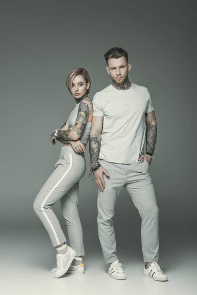 fashionable tattooed couple in sportswear posing together, isolated on grey   - Photo, Image