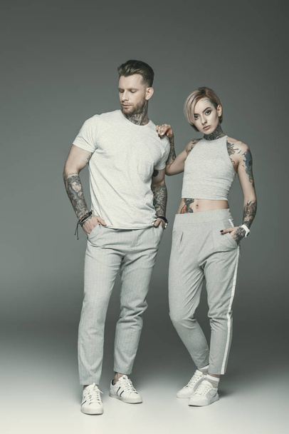 fashionable tattooed couple in sportswear, isolated on grey   - Foto, afbeelding