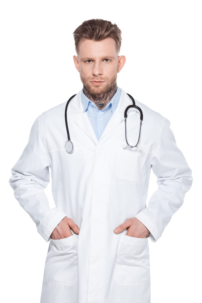 professional doctor with stethoscope and hands in pockets of white coat, isolated on white - Фото, изображение