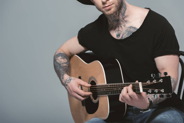 cropped view of tattooed man playing acoustic guitar, isolated on grey - Valokuva, kuva