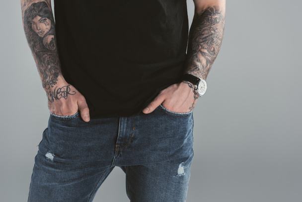 cropped view of tattooed man with watch and hands in pockets, isolated on grey  - Foto, Imagen