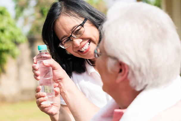 Attenta donna anziana dando una bottiglia d'acqua al suo partner fuori
 - Foto, immagini