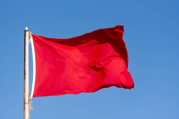 Old red flag and blue sky, red banner waving against blue sky - Fotó, kép