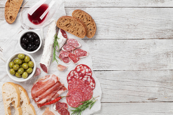 Salami, ham, worst, ham, spek, toast, olijven gesneden. Vlees antipasto schotel en rode wijn op houten tafel. Bovenaanzicht met kopie ruimte - Foto, afbeelding