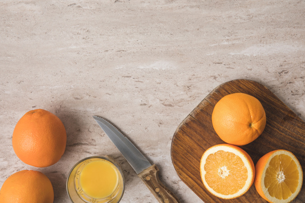 top view of oranges, knife and wooden board on marble surface - 写真・画像
