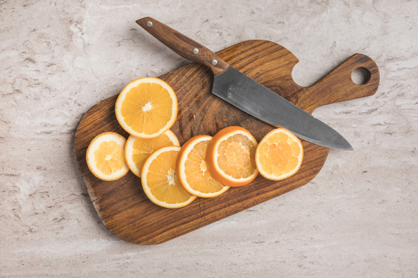top view of cut oranges and knife on wooden board - Foto, Bild