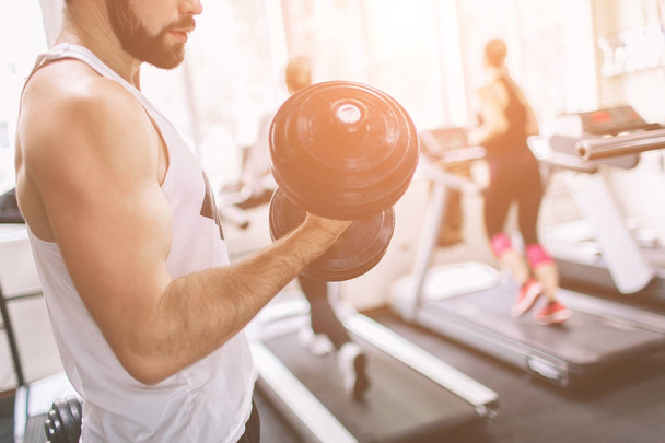 Muscular Bearded man during workout in the gym. Athlete muscular bodybuilder in the gym training biceps with dumbbell. Indoor fitness - Photo, Image