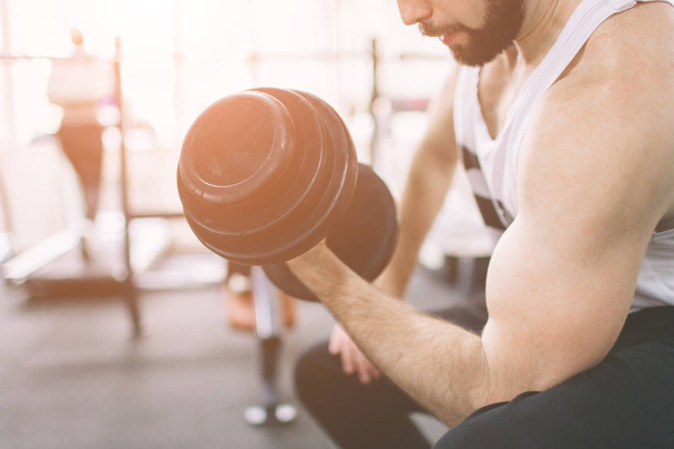 Muscular Bearded man during workout in the gym. Athlete muscular bodybuilder in the gym training biceps with dumbbell. Indoor fitness - Foto, Imagen